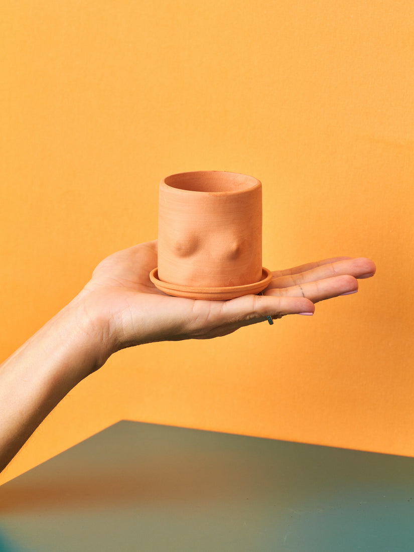 A mini nude terracotta top pot held up in the palm of a hand.