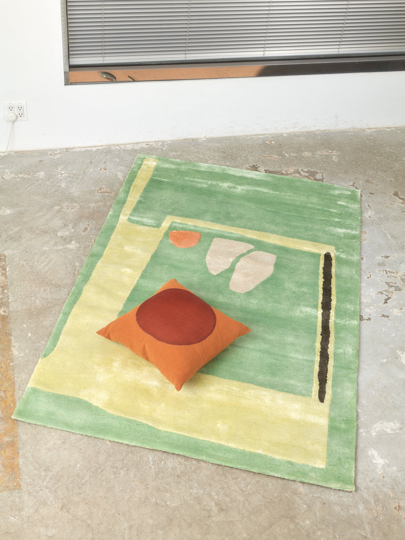A rust colored Velvet Circle Pillow lays on a 4x6 Mochi Rug by Cold Picnic.