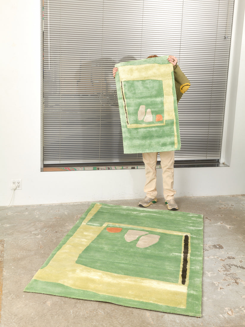 Someone holds up a 2x3 Mochi Rug by Cold Picnic while standing at the back edge of a 4x6 version laying on the floor.
