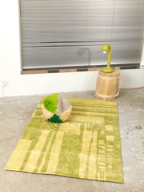 A green Sheepskin Orb Pillow, Green Ceramic Table Lamp on a Rattan Stool, and 4x6 Battenberg in Matcha Rug by Cold Picnic.