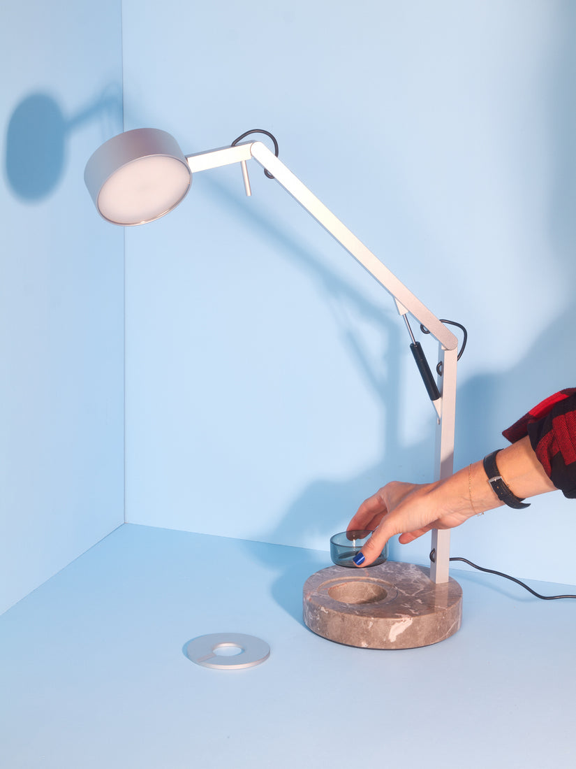 A hand lifts the glass ashtray up from the marble base of the Strut Lamp.