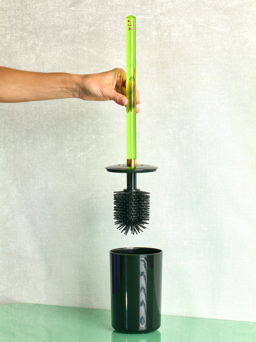 A hand lifts up a green toilet brush by Staff.