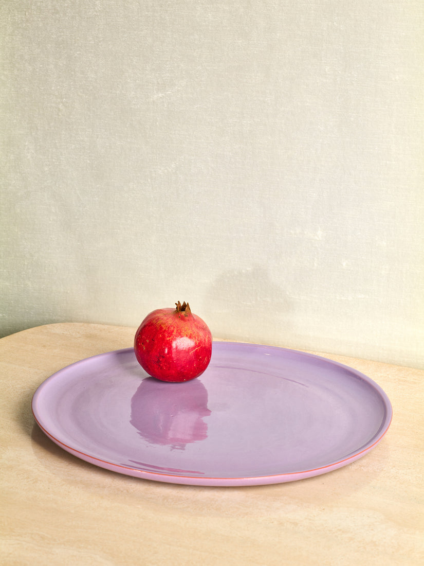 A very large lavender ceramic serving dish with a pomegranate on top.