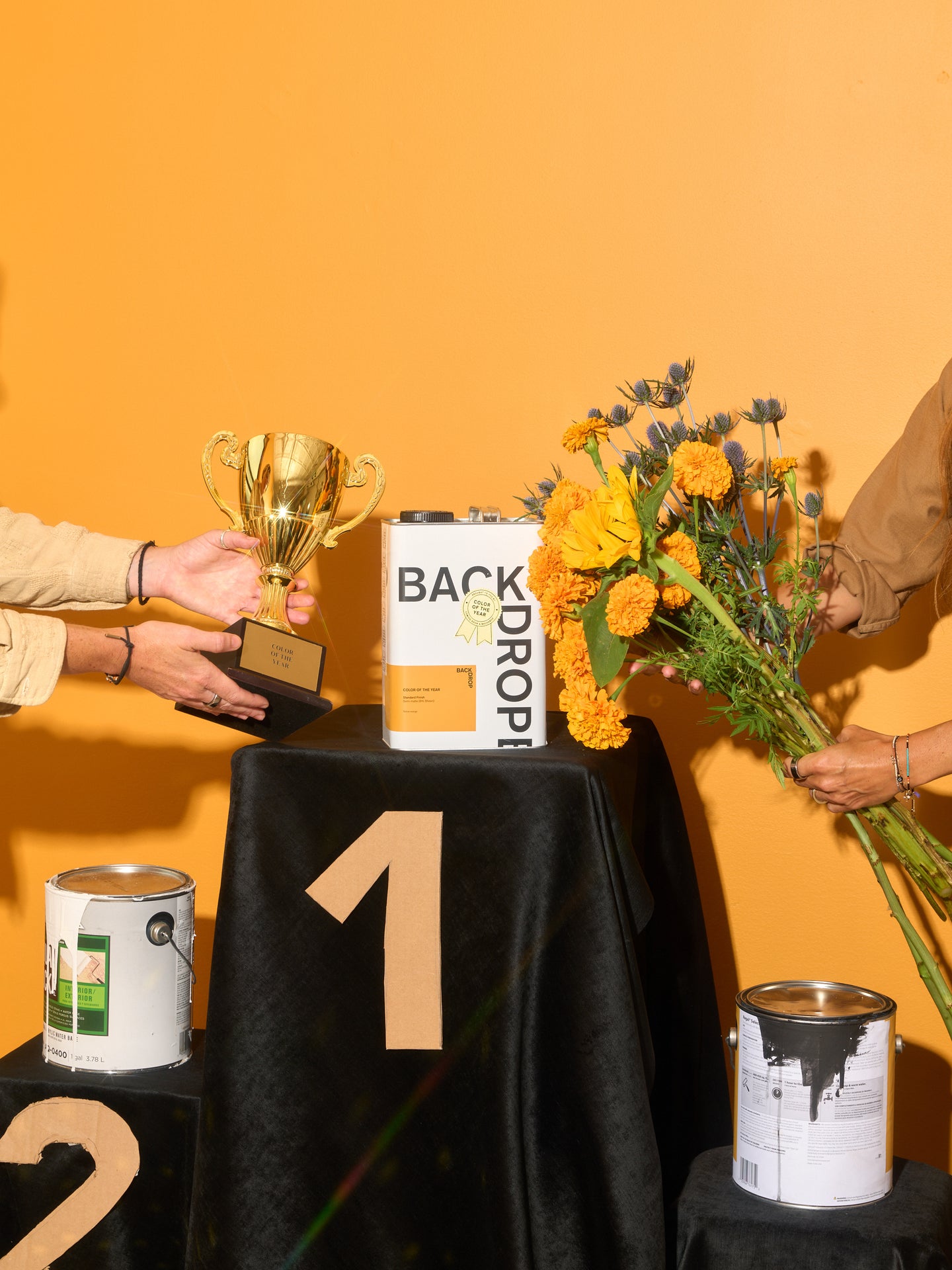 Hands present a trophy and a bouquet of flowers to the paint can.