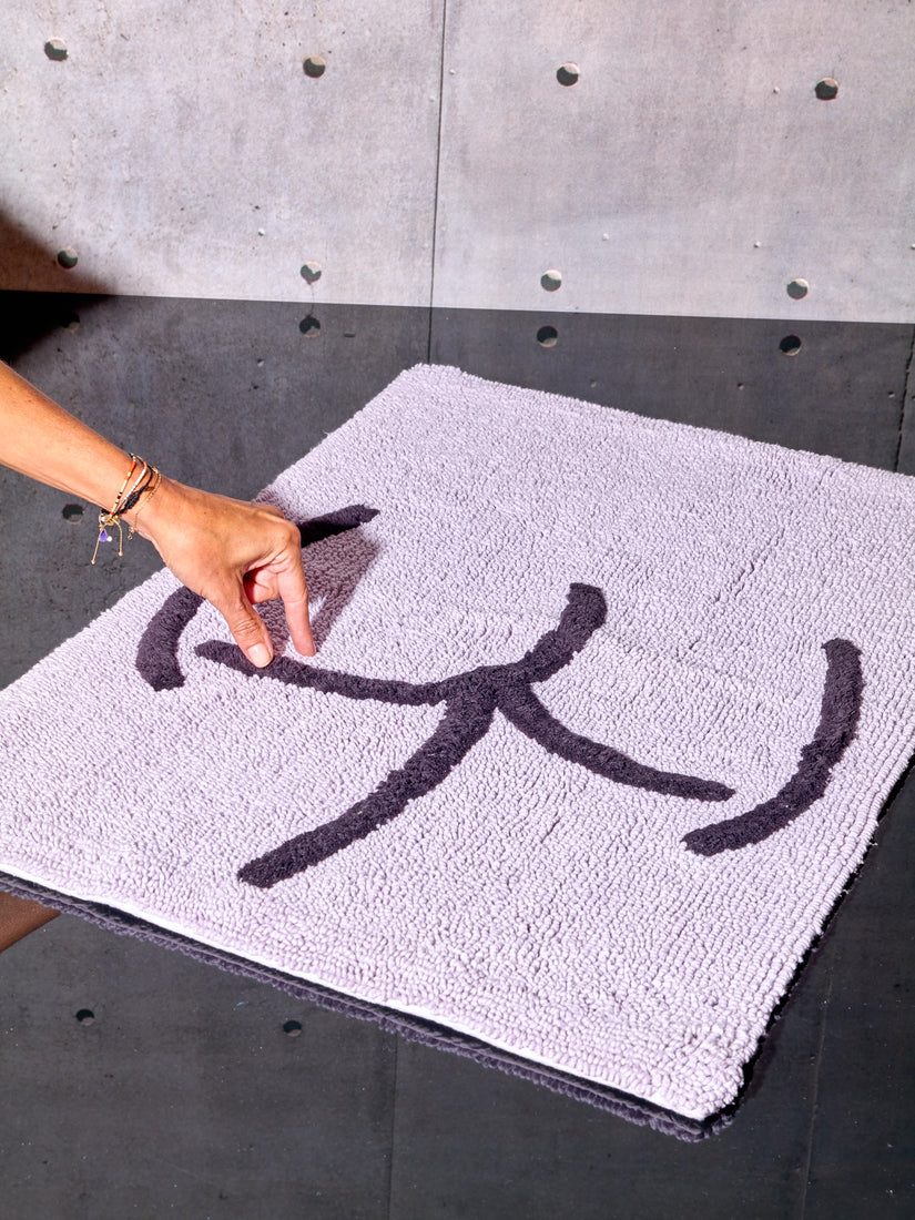 A hand mimics pinching the Tushy graphic on a lavender bath mat.