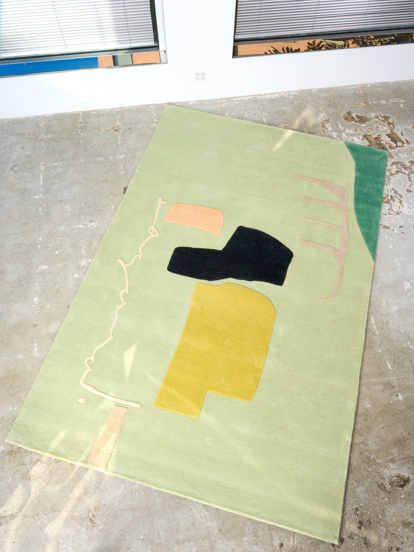 Seafoam green, teal, peach, chartreuse, black, and cream abstract rug on a concrete floor.