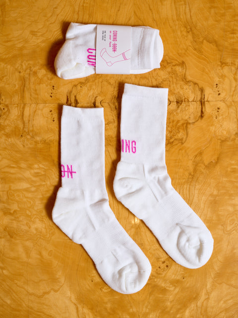 Two pairs of white Coming Soon socks, one in its packaging.