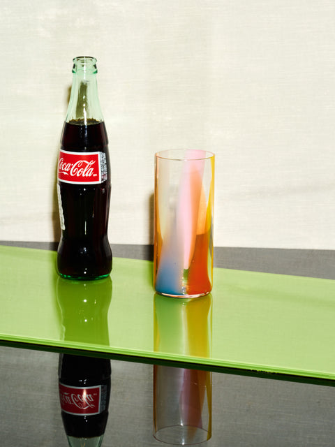 A glass bottle of coke sits left of a Rainbow Splash Highball by Bow Glass.
