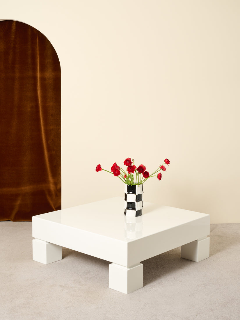 A Bamboo Vase full of red flowers sits atop the white lacquered coffee table.