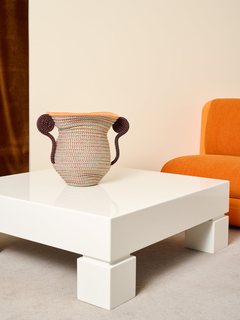 A giusti urn sits atop the lacquered coffee table that sits in front of an orange Uma T4 chair.