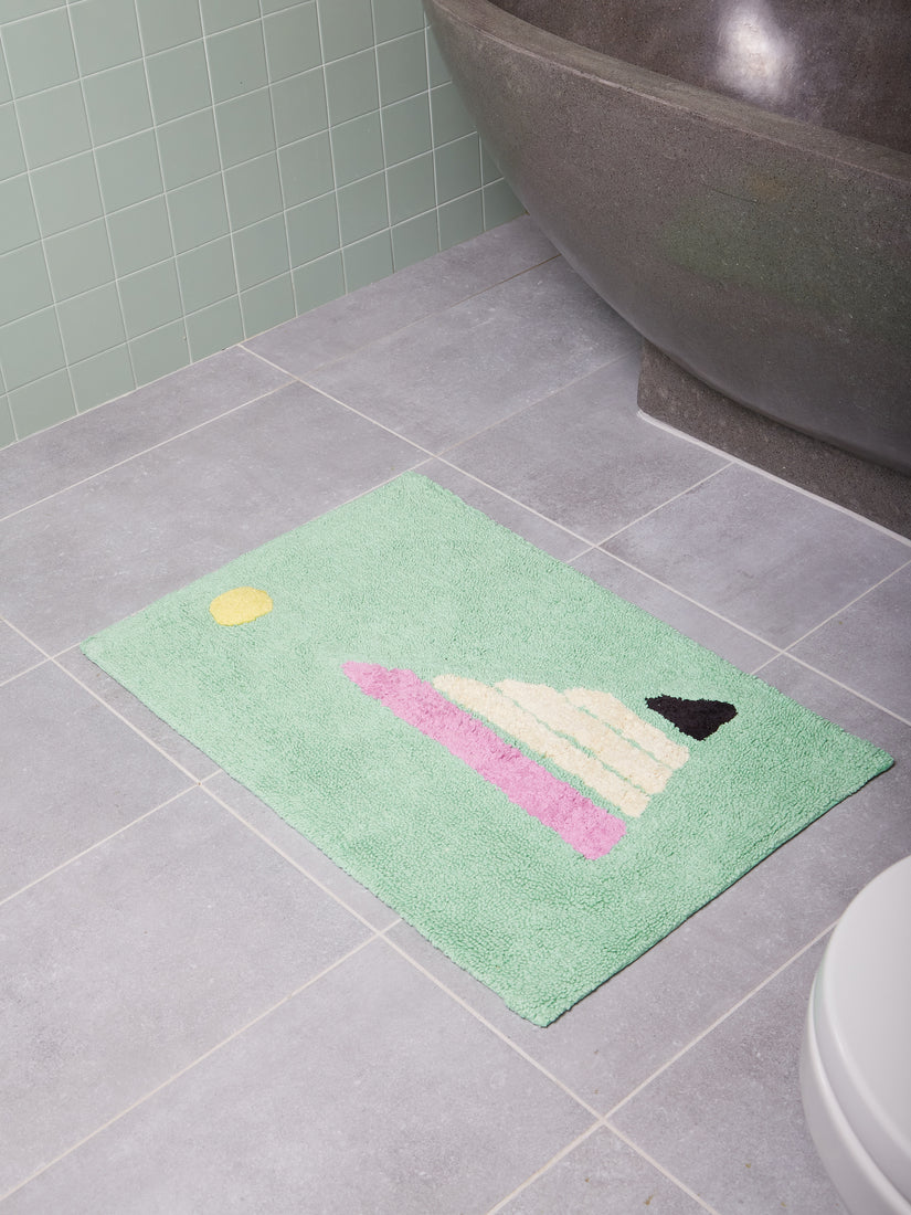 A mint green bath mat featuring an abstract design of yellow, lilac, cream, and black.