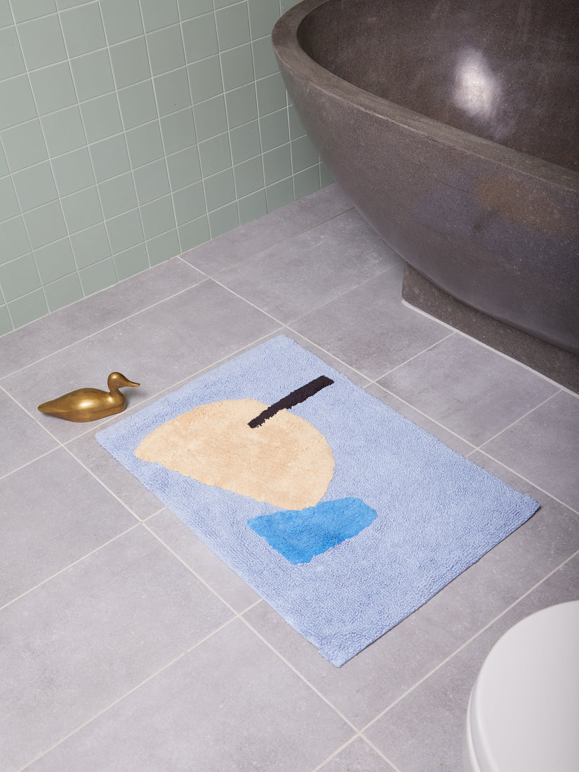 The Cool Breeze Bath Mat by Cold Picnic in a grey bathroom.