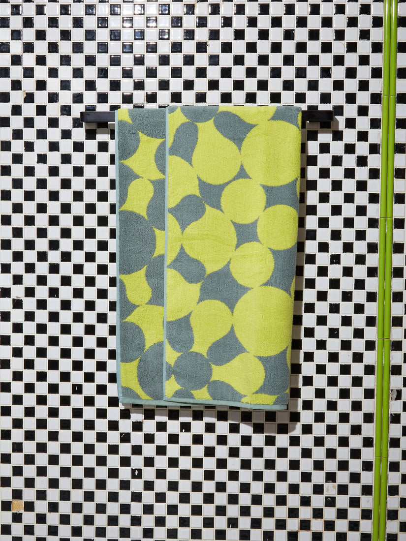 A Penrose Bath Towel by Dusen Dusen hung on a black towel rack against a checkered tiled wall.