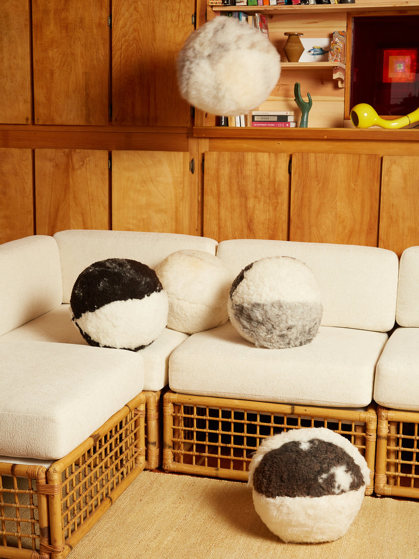 White and grey tone Sheepskin Pillows by Casa Ahorita surround a white cushioned rattan couch. 
