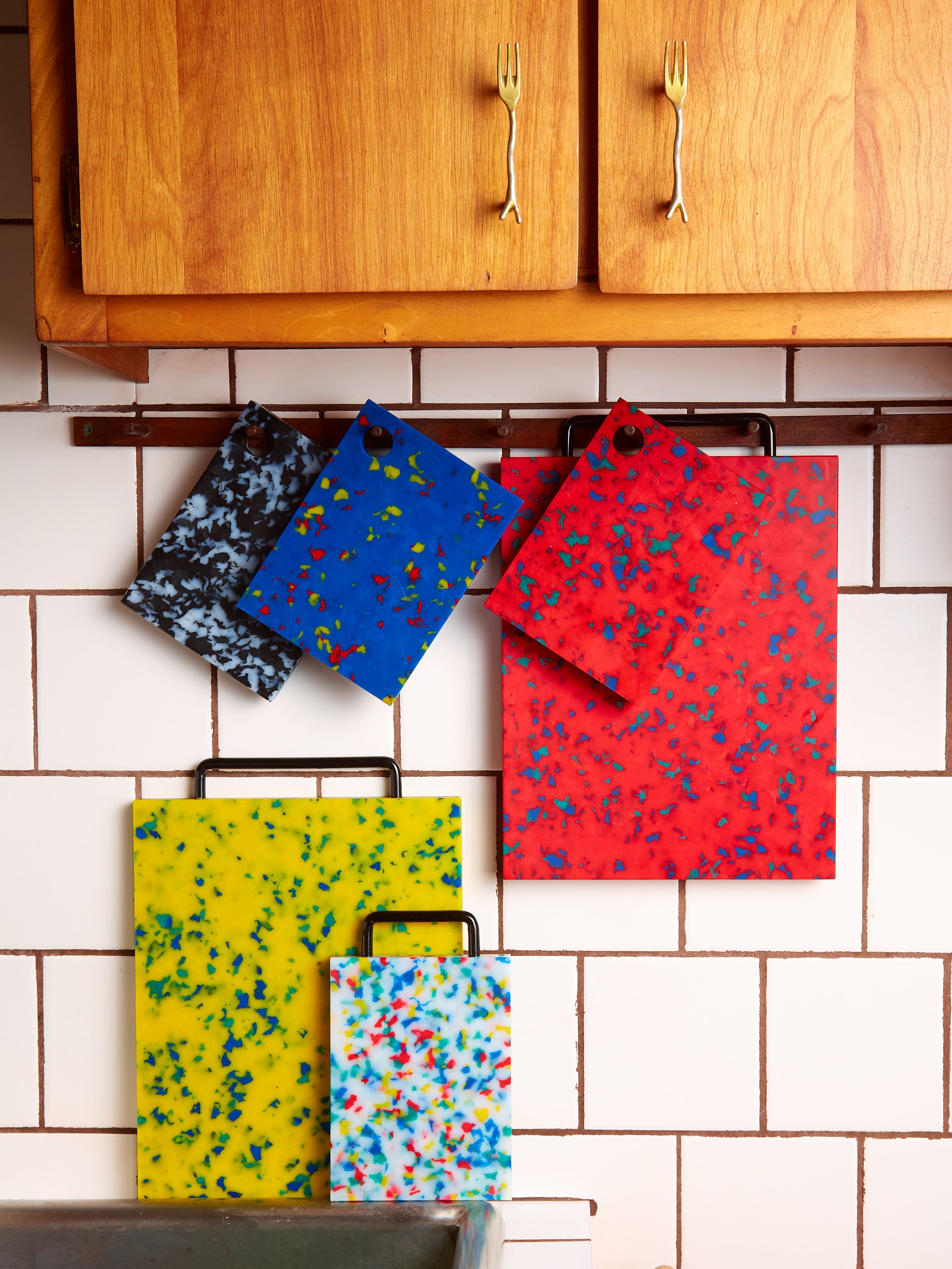 A kitchen rack with 3 small chopping blocks in different colors with a full sized red block hanging above a full sized yellow block and small multicolor block.