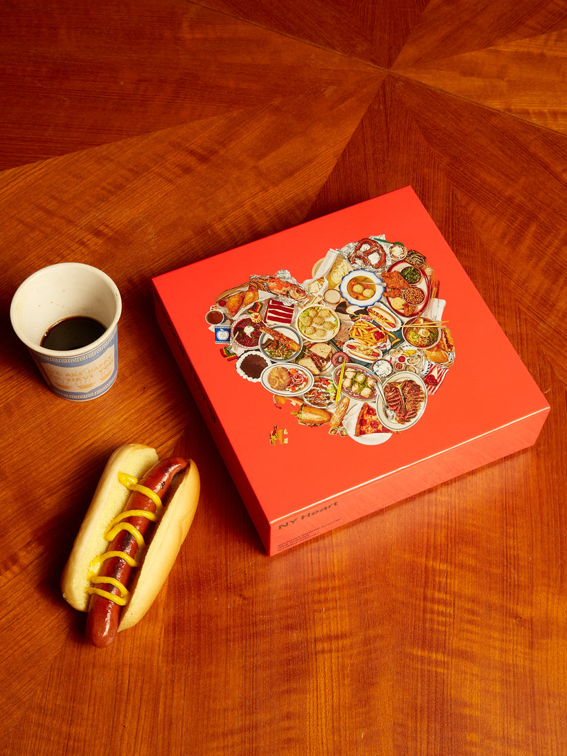The NY Heart Puzzle by Areaware pictured next to a cup of coffee and a dressed hot dog.
