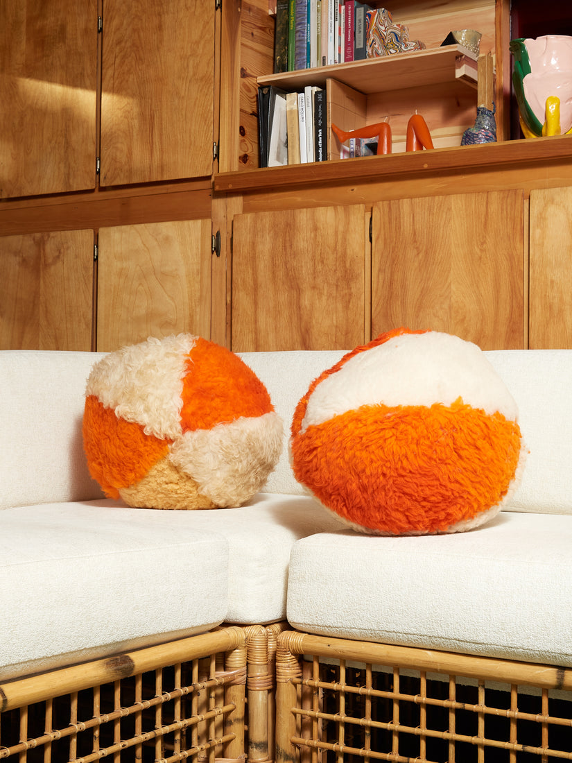 A pair of Orange and Cream Sheepskin Orb Pillows sit atop white cushions.