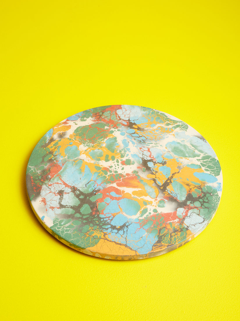 A concrete lazy susan with rainbow multicolor pattern against a bright yellow background.