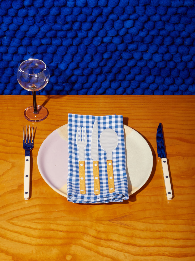 A place setting with a wine glass, ceramic plate, fork and knife, and a La Serviette Napkin by Steak Diane.