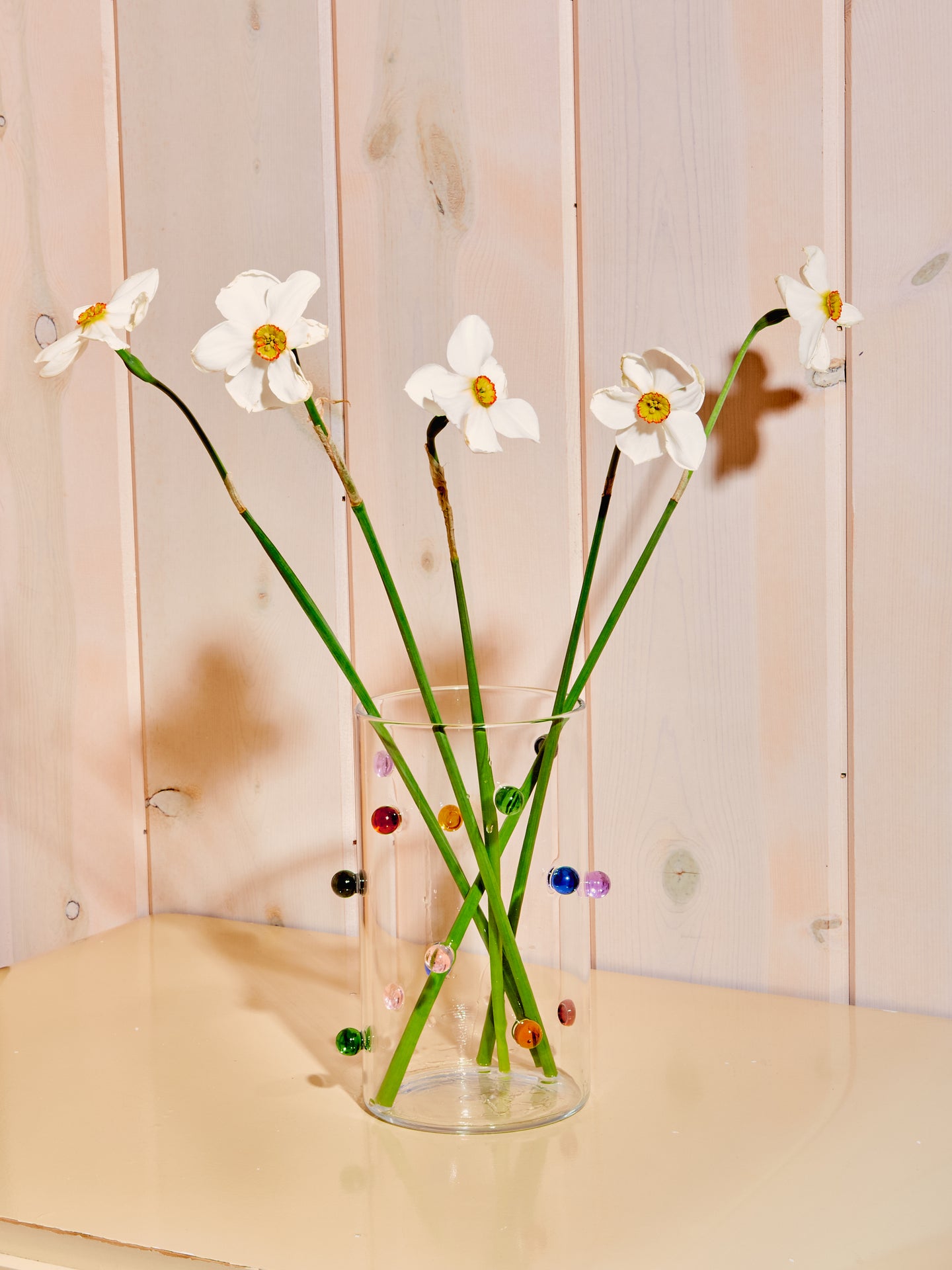 Clear vase with multicolored glass orbs along its exterior.