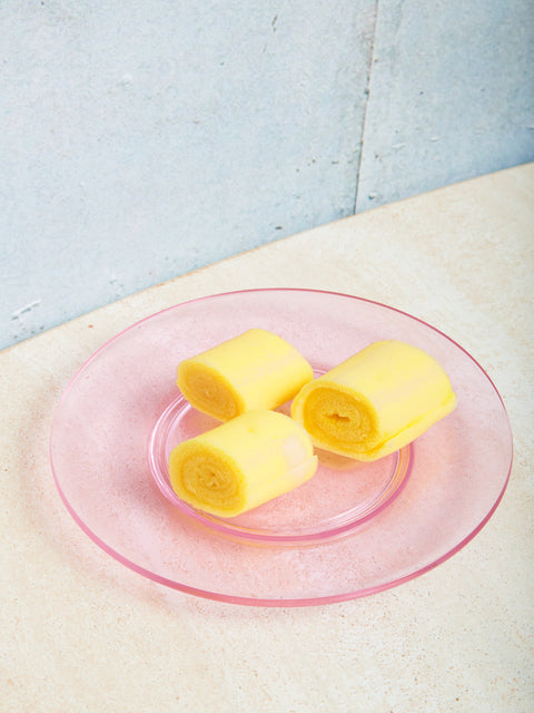 A pink glass plate with three rolled desserts on top.