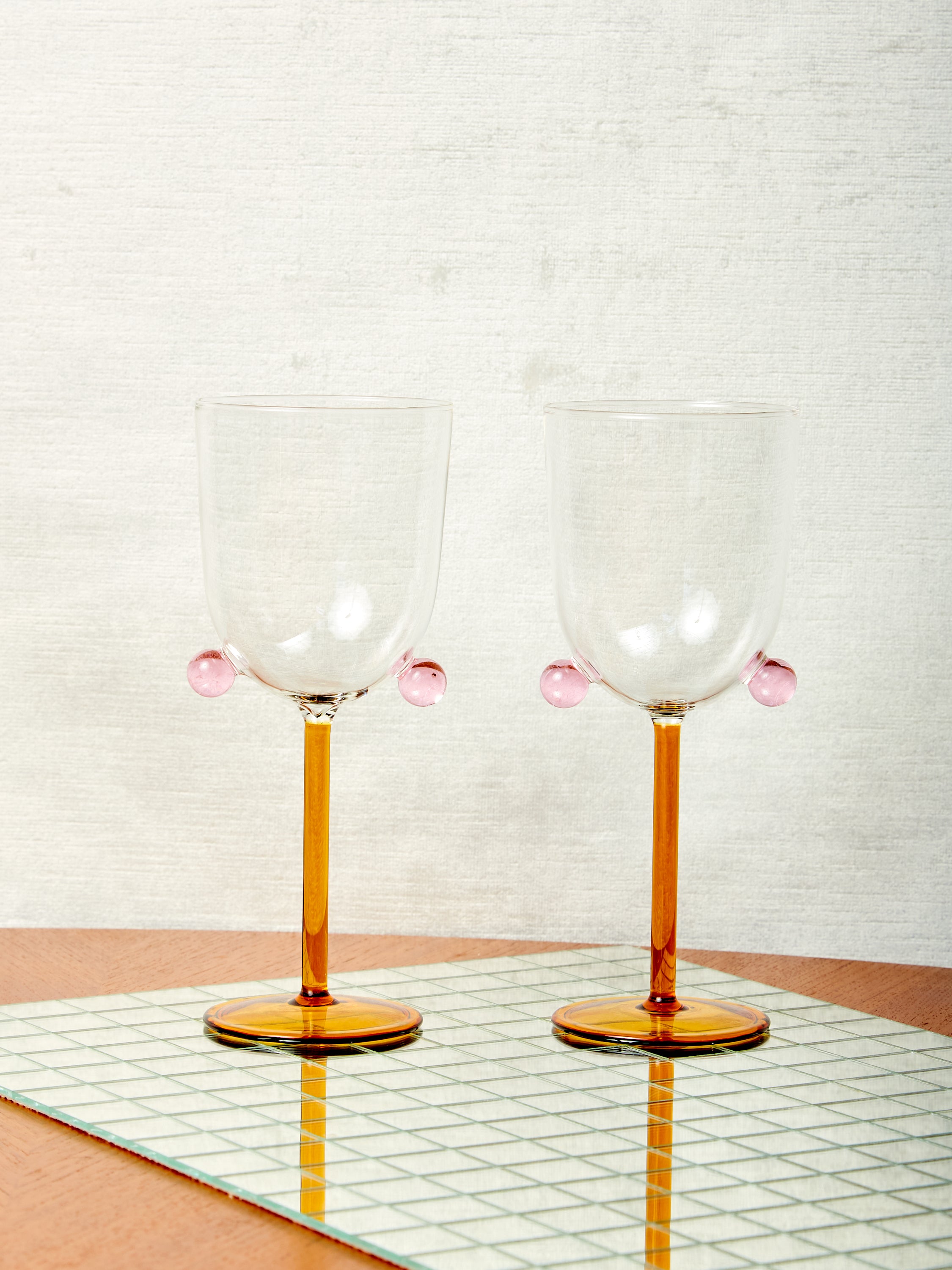 A pair of honey and pink Pompom Wine Glasses by Maison Balzac.