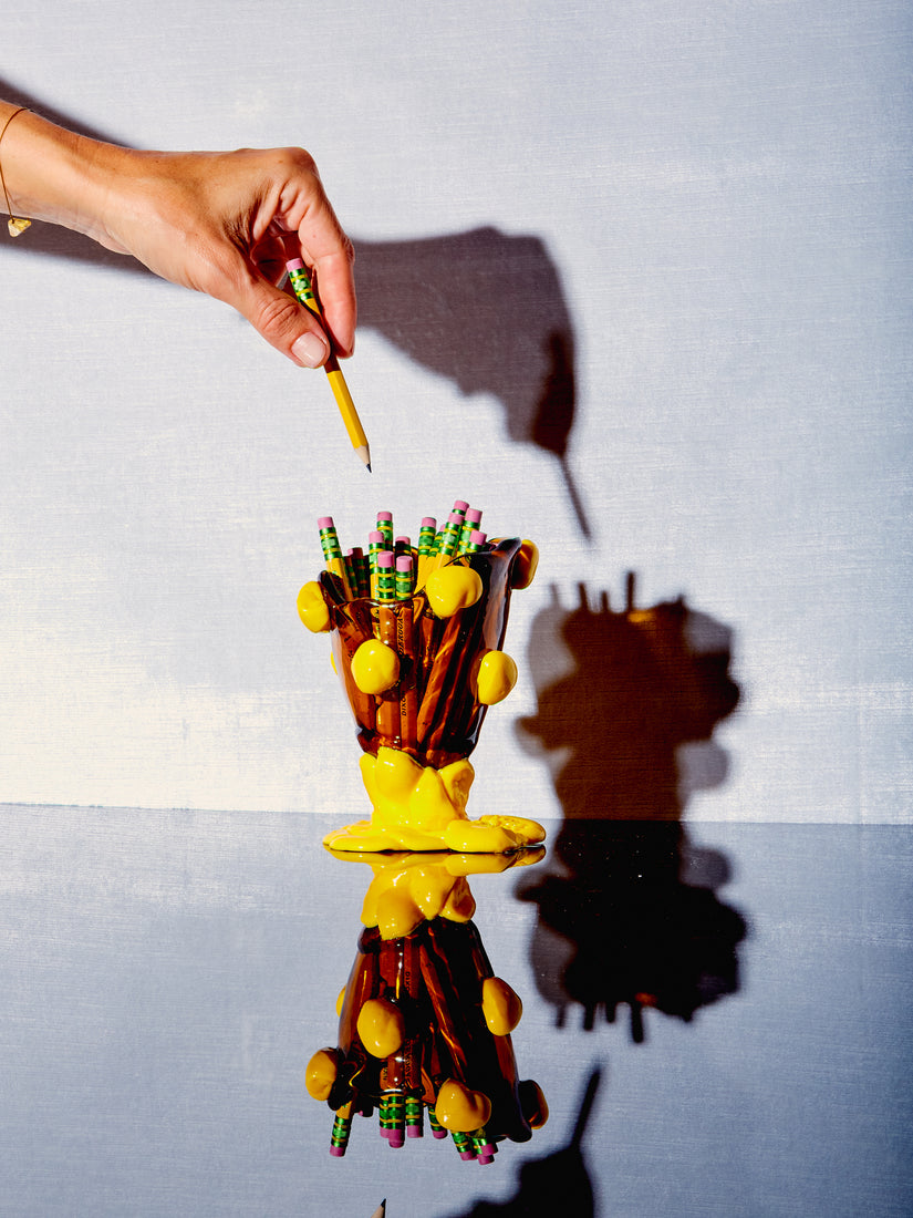 A mini nugget vessel in brown full of mini yellow pencils.