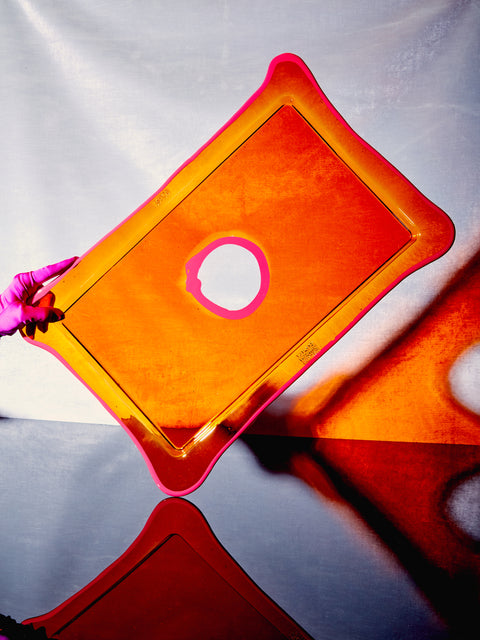 A hand holds the Large Rectangular Tray in Orange/Fuchsia up on its corner.