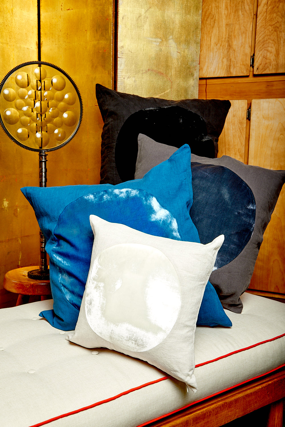 A black, charcoal, blue, and ivory Velvet Circle Pillow by Correll Correll piled up on a white daybed.