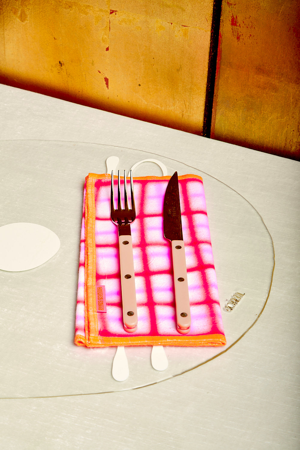 Pastel peach flatware sits atop a folded bright red, pink, and orange dinner napkin by Hotel Elma.