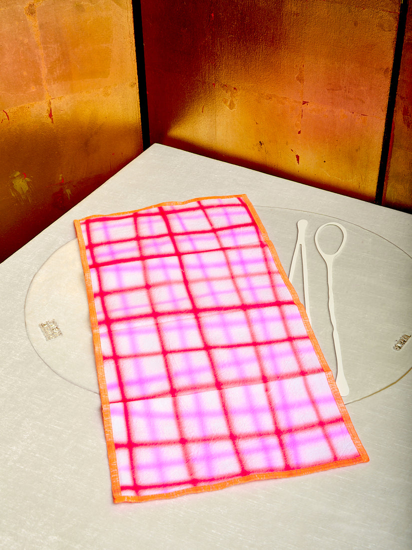 A vibrant red and neon pink napkin by Hotel Elma with neon orange trim is draped across a transparent placemat by Gaetano Pesce for Fish Design.