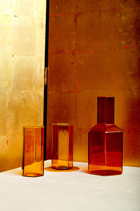 An amber Coucou Decanter sits next to a pair of matching Coucou Glasses.