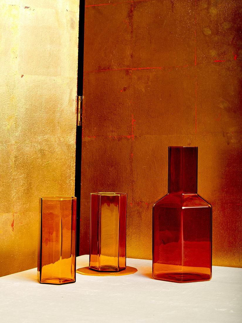 An amber Coucou Decanter sits next to a pair of matching Coucou Glasses.
