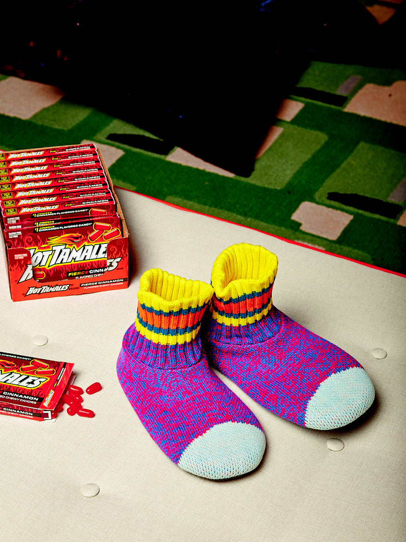 A pair of red/blue sock slippers by Verloop next to a case of Hot Tamales candies.
