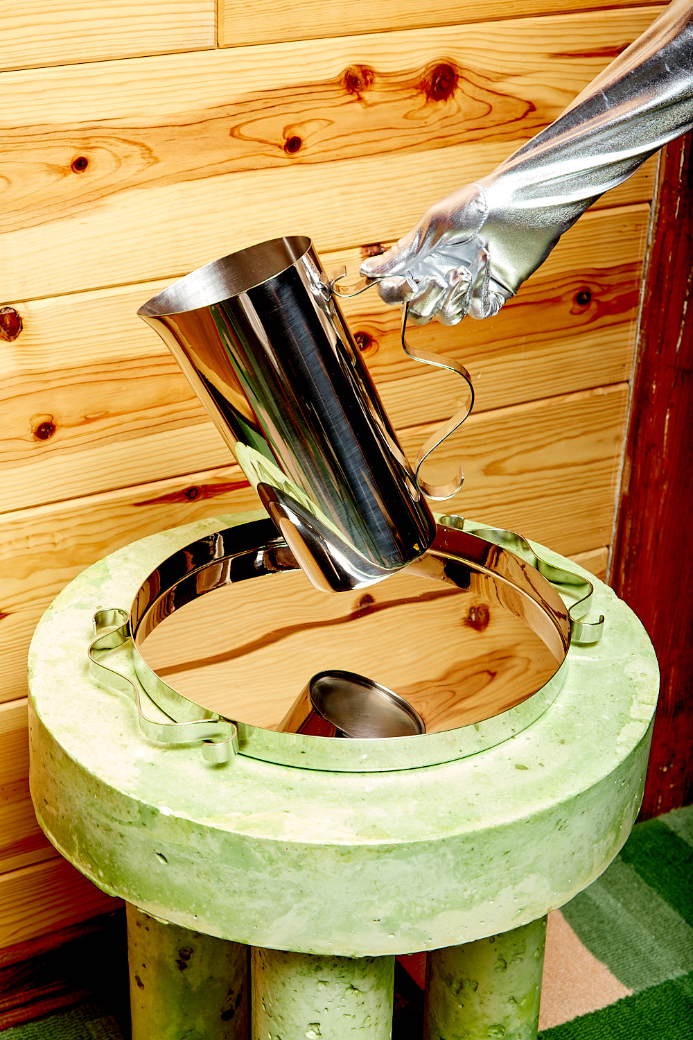 Squiggle Pitcher being held over a Squiggle Tray by a silver gloved hand.