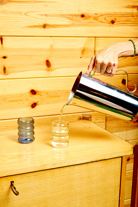 A hand pours water from the Sophie Lou Jacobsen Squiggle Pitcher into ripple glasses.