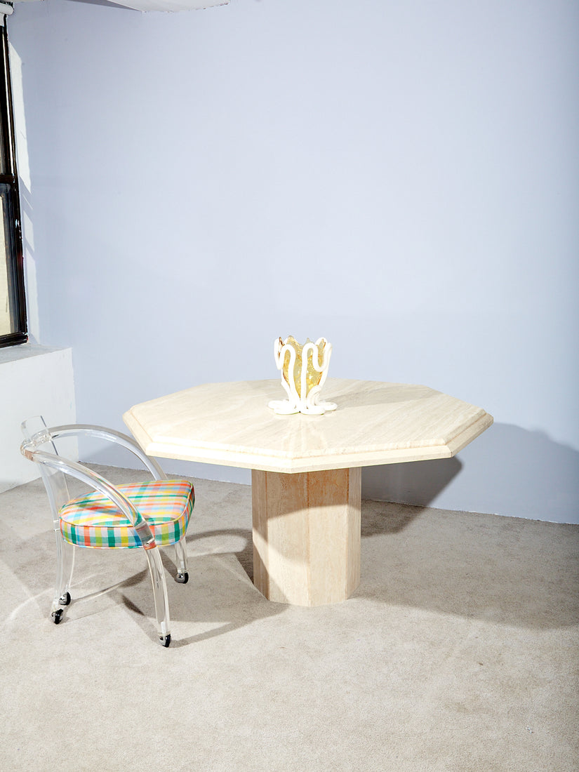 A lucite loop chair pulled up to the Travertine Dining Table.