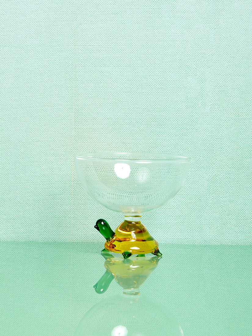 A clear glass bowl that's base is a yellow and green glass turtle.