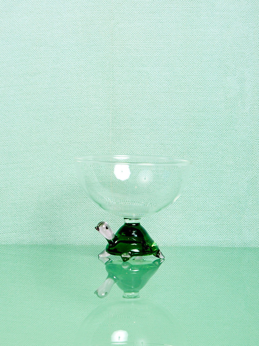 A clear glass bowl thats base is a green and pink glass turtle.