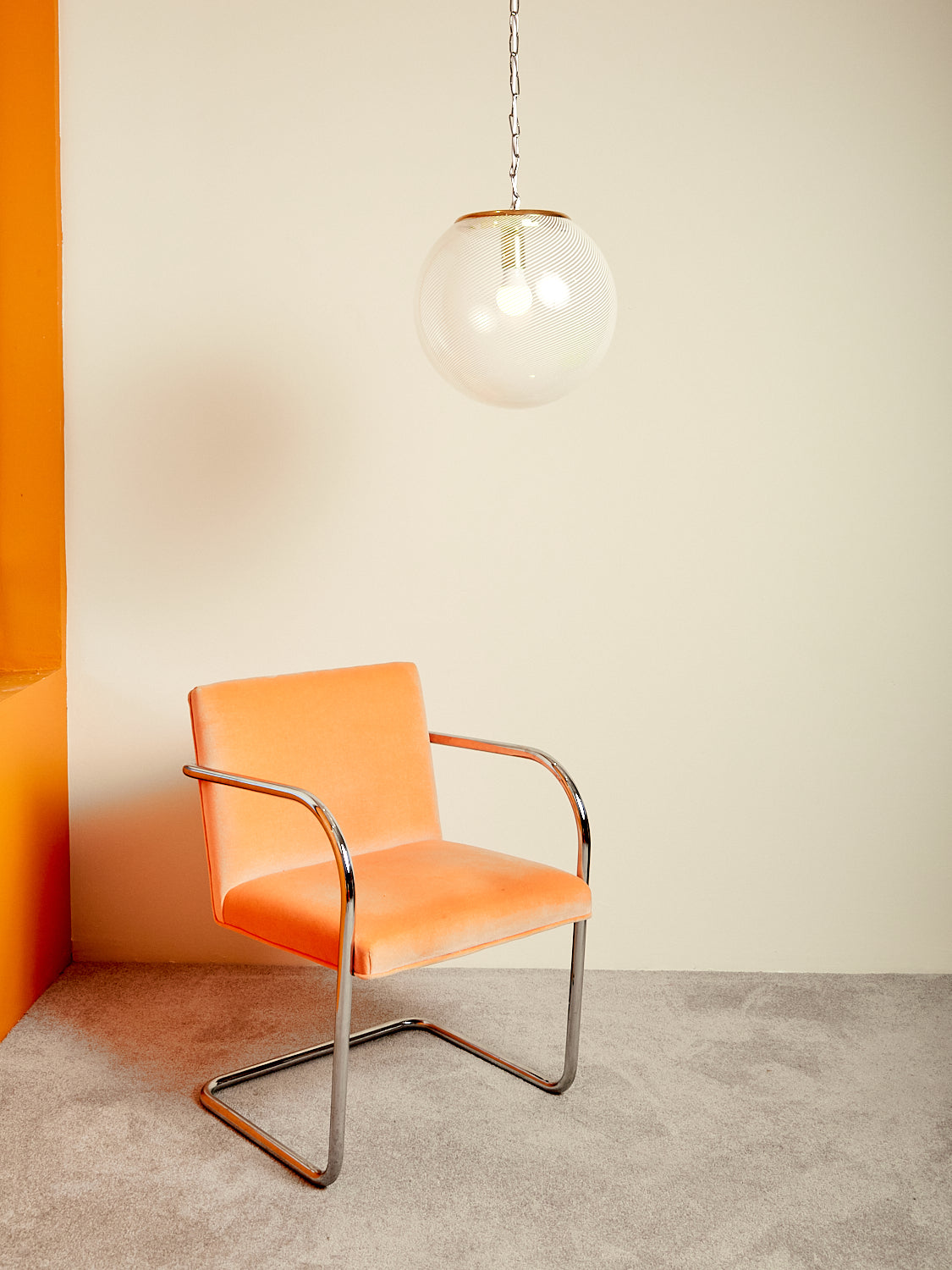 The Lattimo Glass Pendant Lamp hanging over a tangerine Brno chair.