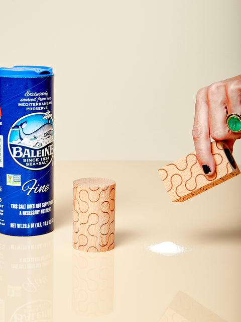 A hand holds up the square shaker from the Pattern Shakers by Dusen Dusen pouring out a small pile of salt.