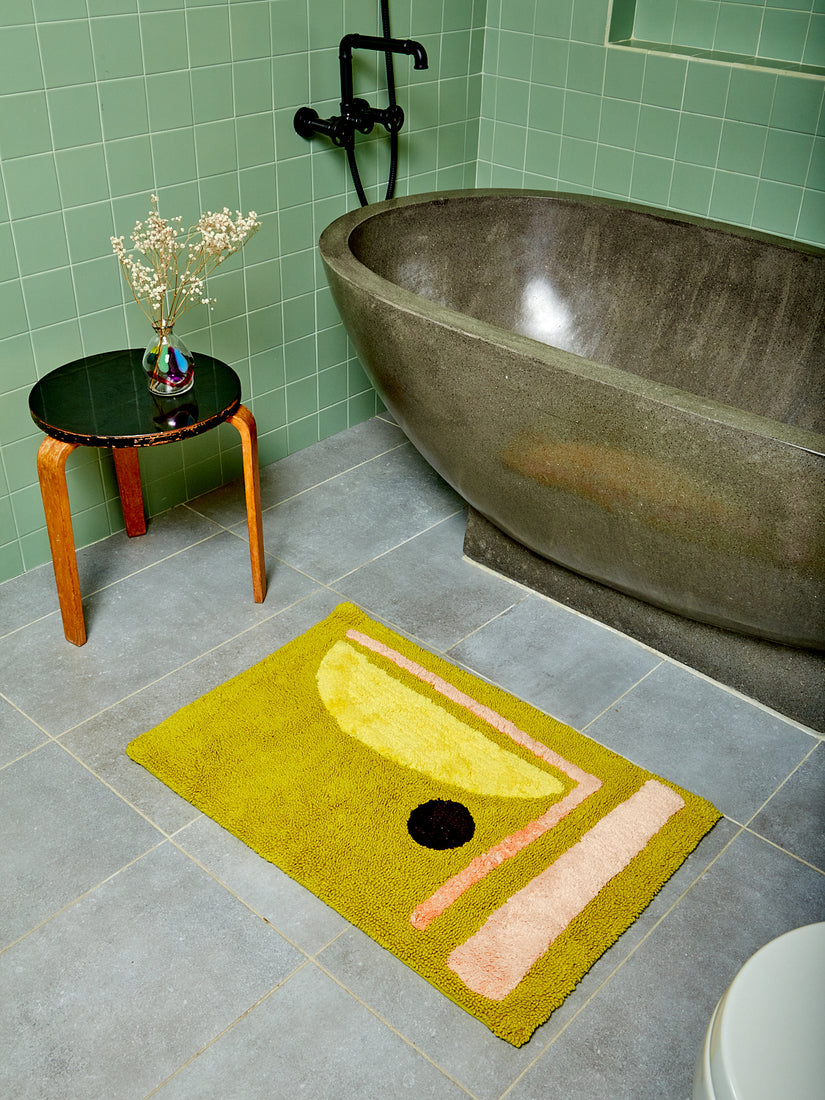 A booger green bath mat with abstract design by Cold Picnic styled in a tiled bathroom.