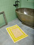 The Frames Bath Mat by Cold Picnic sits in a sage green tiled bathroom in front of a rounded stone bathtub.