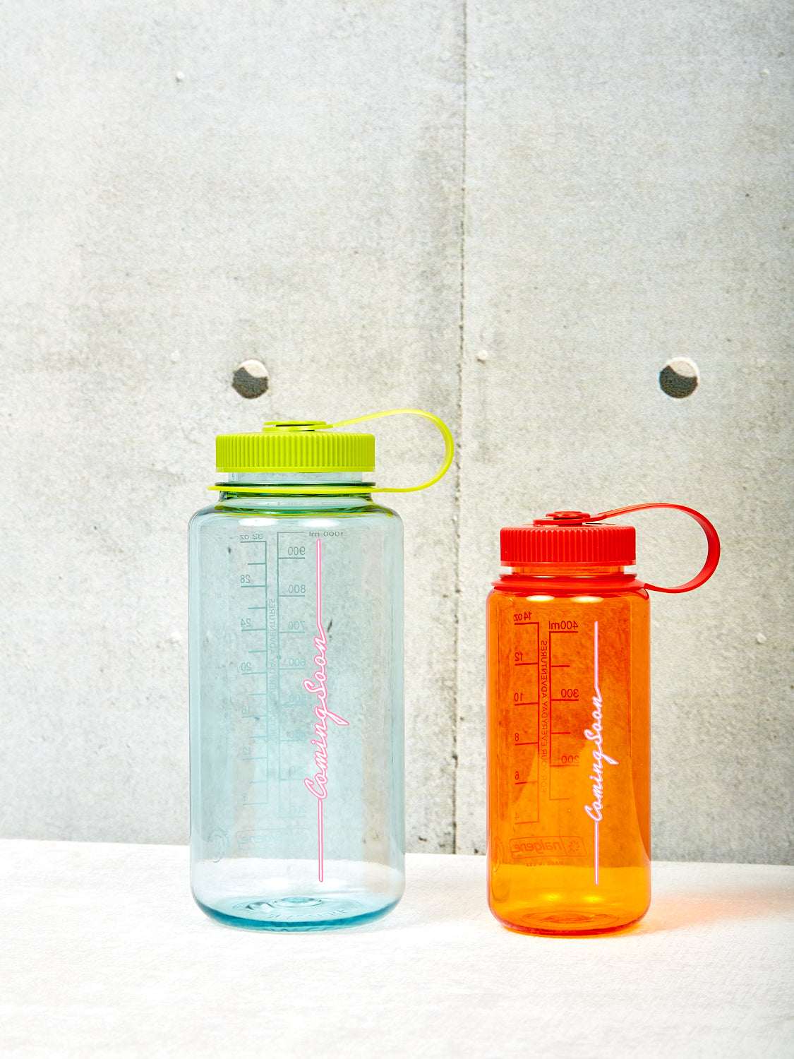 A large Coming Soon Nalgene in Seafoam green and a small Coming Soon Nalgene in orange.