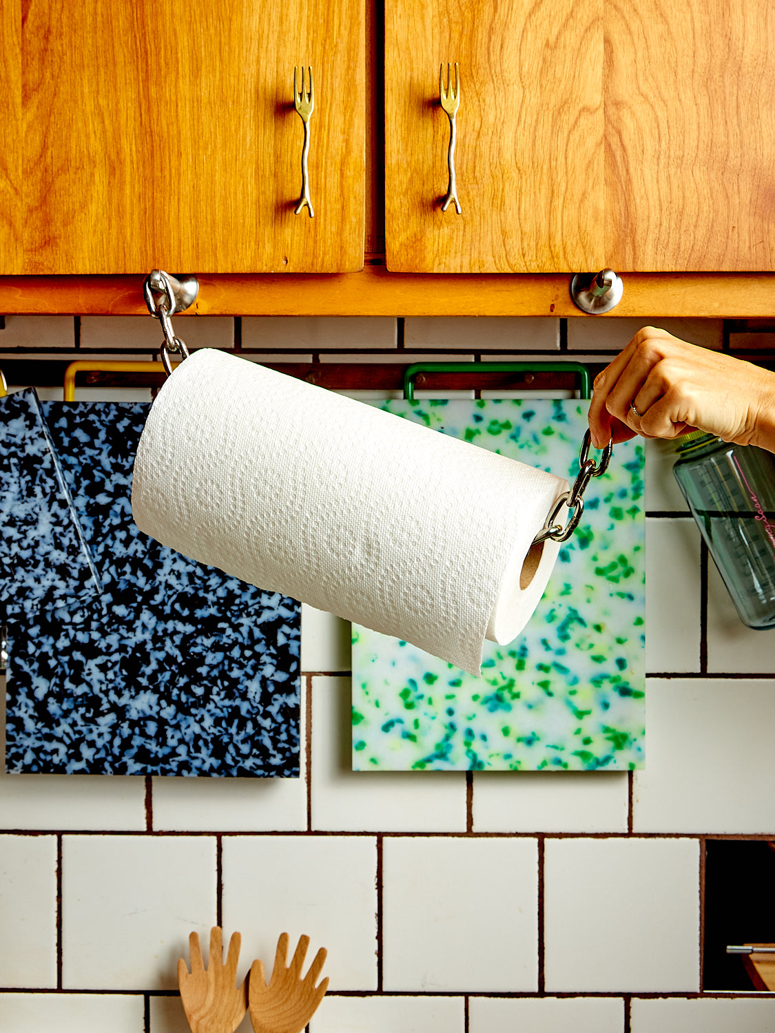 A hand pulls one end of the chain off a Catena Paper Towel Holder.