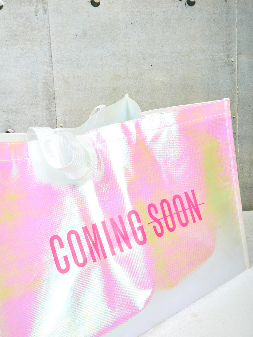 A close up of the hot pink Coming Soon logo on the front of the iridescent tote bag.