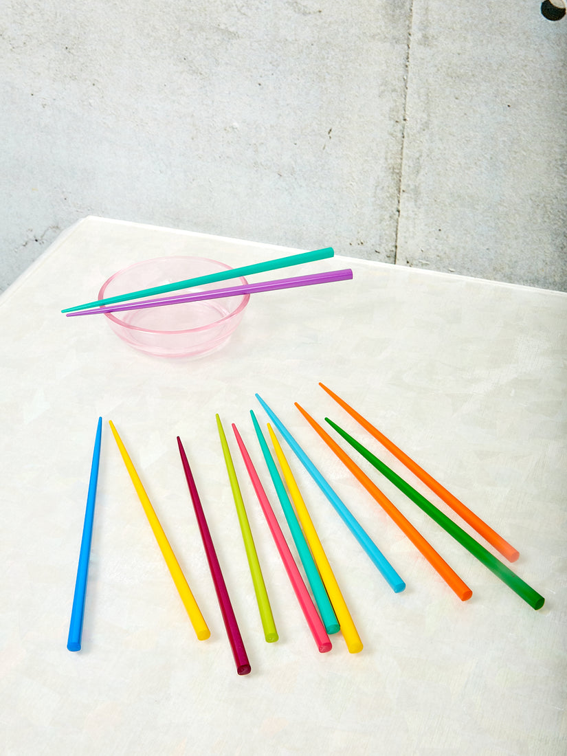 Rainbow Chopsticks by Moma splayed out on a table top, a pair of teal and purple chopsticks rests on a small pink bowl.