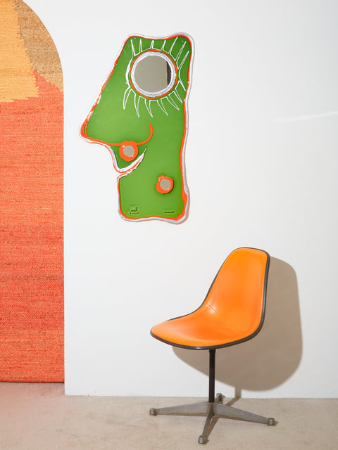 A mostly transparent green resin mirror with 3 round mirrors that make up an abstract face design. Outlined by opaque orange and silver resin.