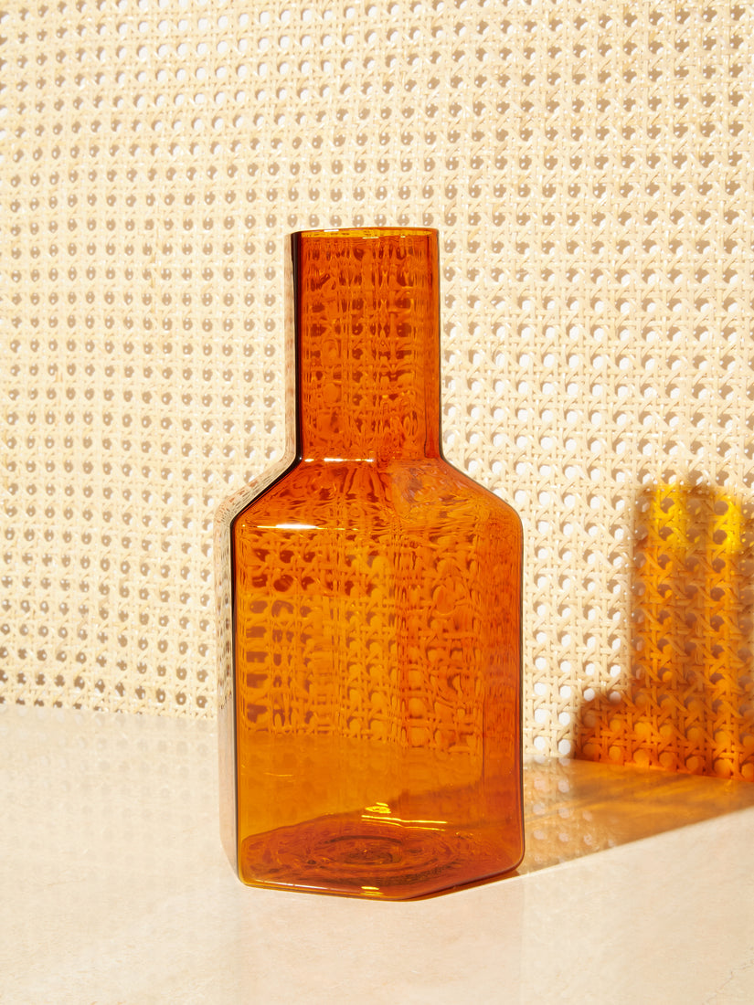 An amber Coucou Decanter by Maison Balzac on a rattan backdrop.