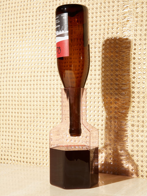 A bottle of red wine sits upside down in a pink Coucou Decanter showing it's contents inside the decanter.